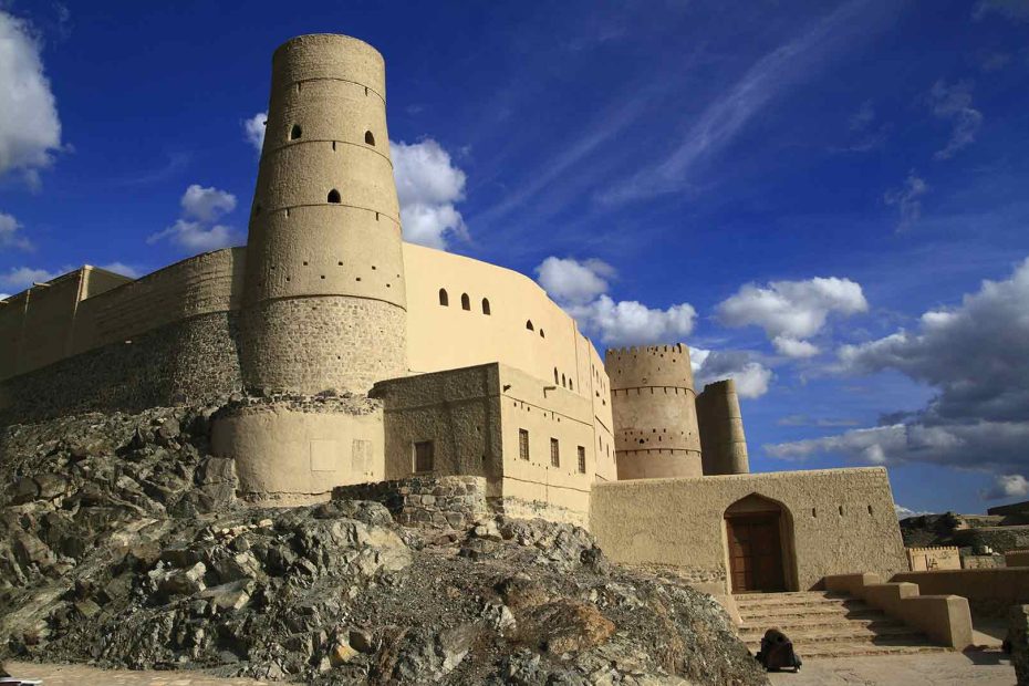 Bahla Fort in Oman, a historic structure and one of the most iconic cultural heritage sites Oman offers, standing tall against a backdrop of clear blue skies and rugged landscape.