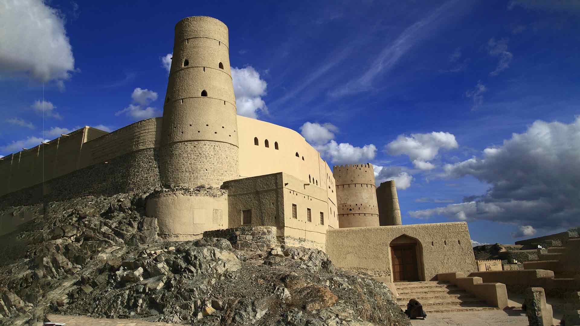 Bahla Fort in Oman, a historic structure and one of the most iconic cultural heritage sites Oman offers, standing tall against a backdrop of clear blue skies and rugged landscape.