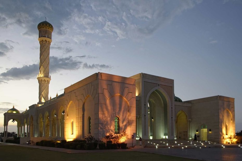 The beautifully illuminated Muscat Mosque at dusk, showcasing its elegant architecture and peaceful surroundings.