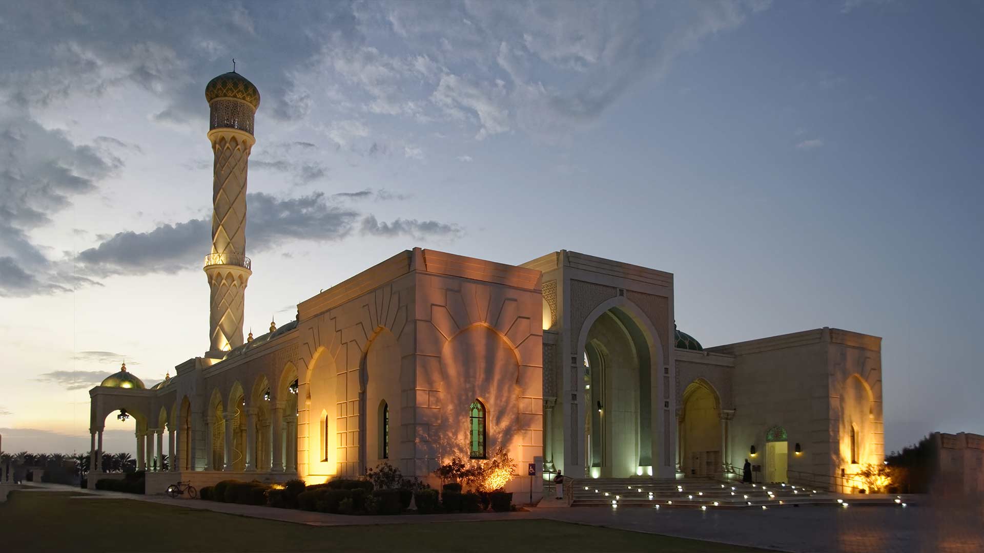 The beautifully illuminated Muscat Mosque at dusk, showcasing its elegant architecture and peaceful surroundings.