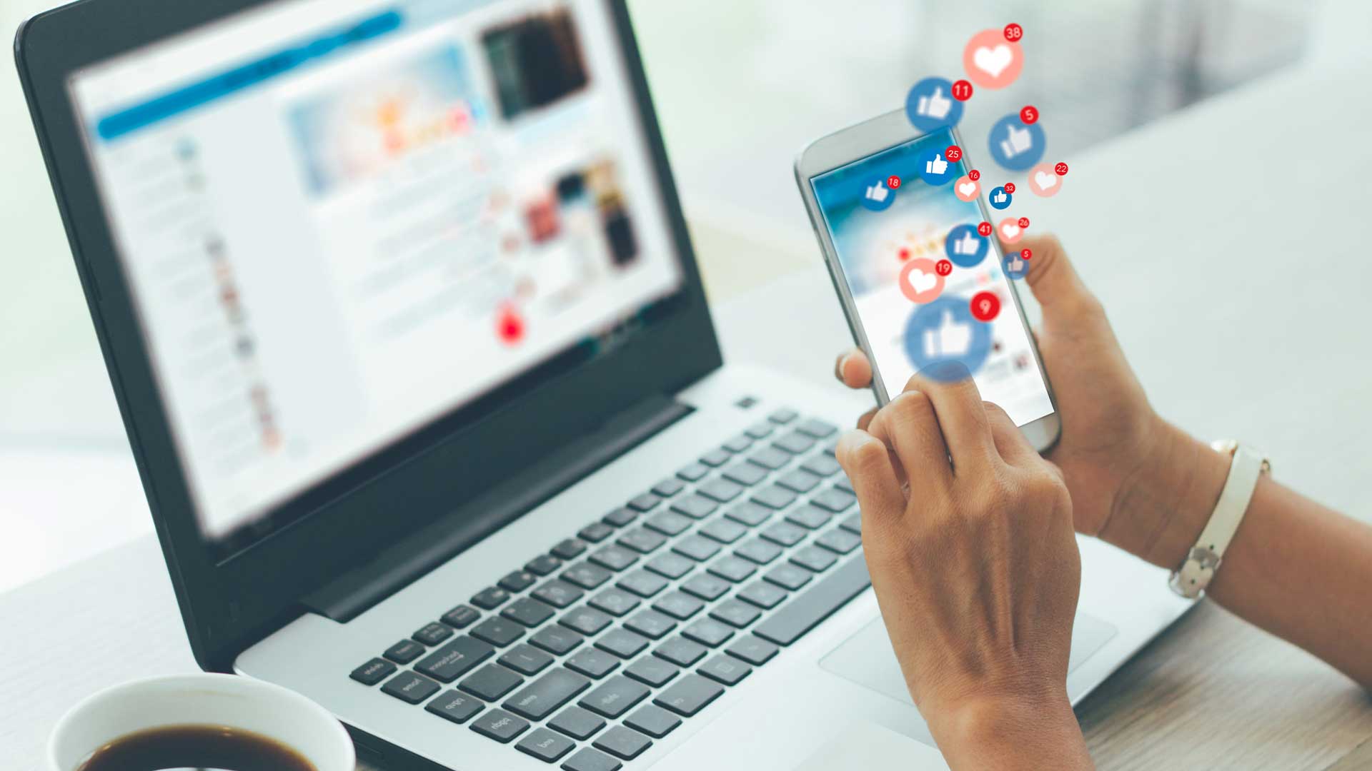 Person using a smartphone with social media notifications while a laptop displays a social media feed, representing the social media influence on Oman businesses.